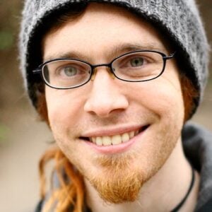 Portrait of Derek, white face with broad smile and glasses.